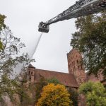 Zdjęcie zamku od strony ulicy Starościńskiej. Z wysokiego wysięgnika pomiędzy koronami drzew strażacy wykonują próbę gaszenia ognia w południowo wschodnim narożniku zamku.