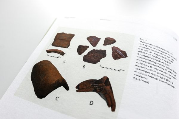 Strona książki ze zdjęciami i opisem fragmentów dachówek.
