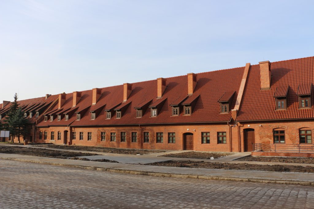 Ciąg budynków z czerwonej cegły przykrytych spadzistym dachem.