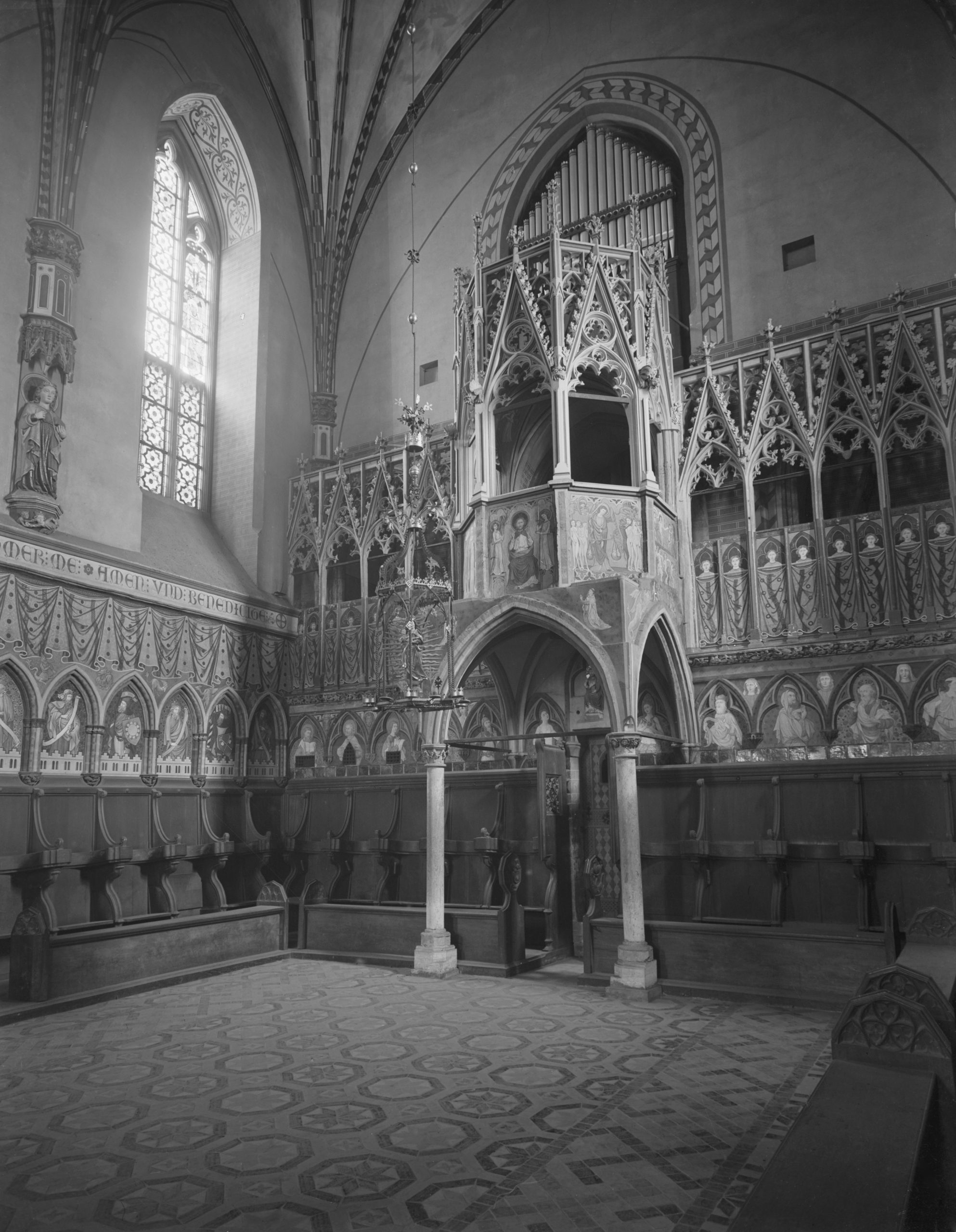 Black-and-white interior of Gothic chapel showing ornate carved pulpit, organ pipes, vaulted ceiling, and choir stalls.